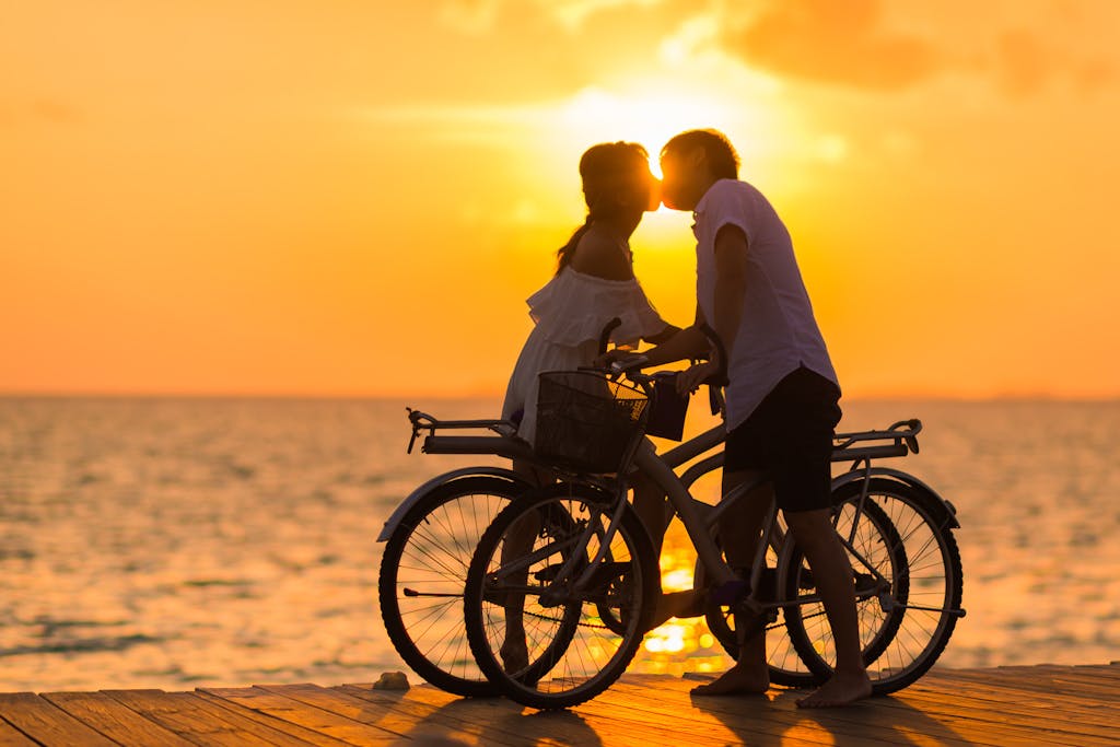 A couple shares a romantic kiss on bicycles during a beautiful sunset at the beach.